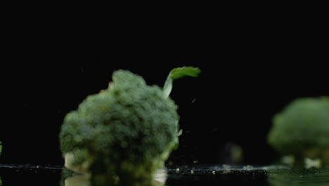 Three-fresh-green-broccoli-fall-on-a-glass-with-splashes-and-drops-of-water-in-slow-motion.-Ingredients-for-Salad-Healthy-Food.